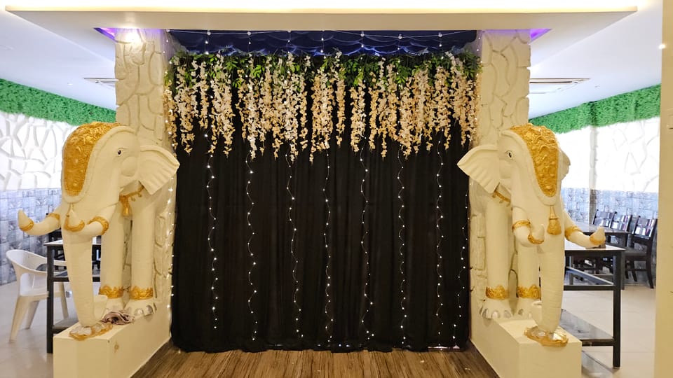 White elephants in gold headdresses flanking a dark drape hung with white blossom and strings of fairy lights