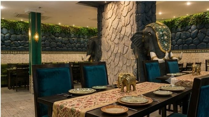 Long family dining table with teal velvet chairs and brass elephant centrepieces at Rasa Raya