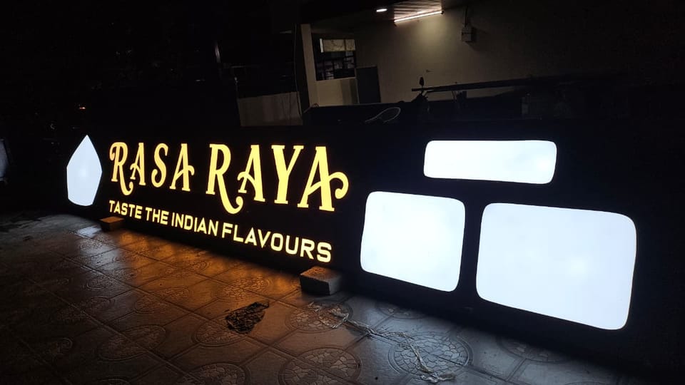 Illuminated Rasa Raya signboard glowing gold at night with the tagline Taste the Indian Flavours